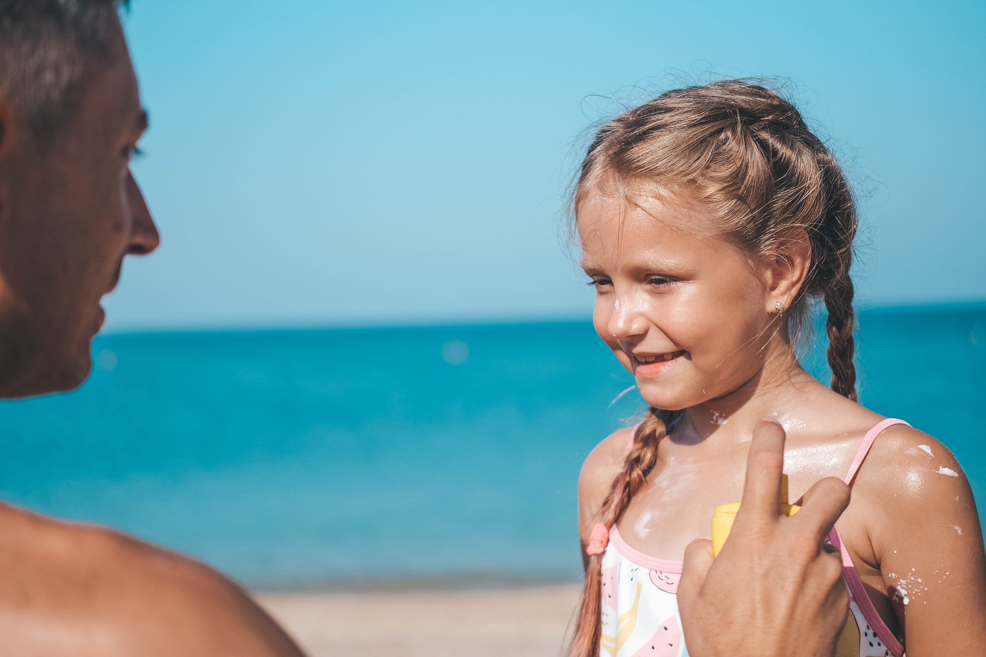 A father applies protective cream to his daughter's body on the beach