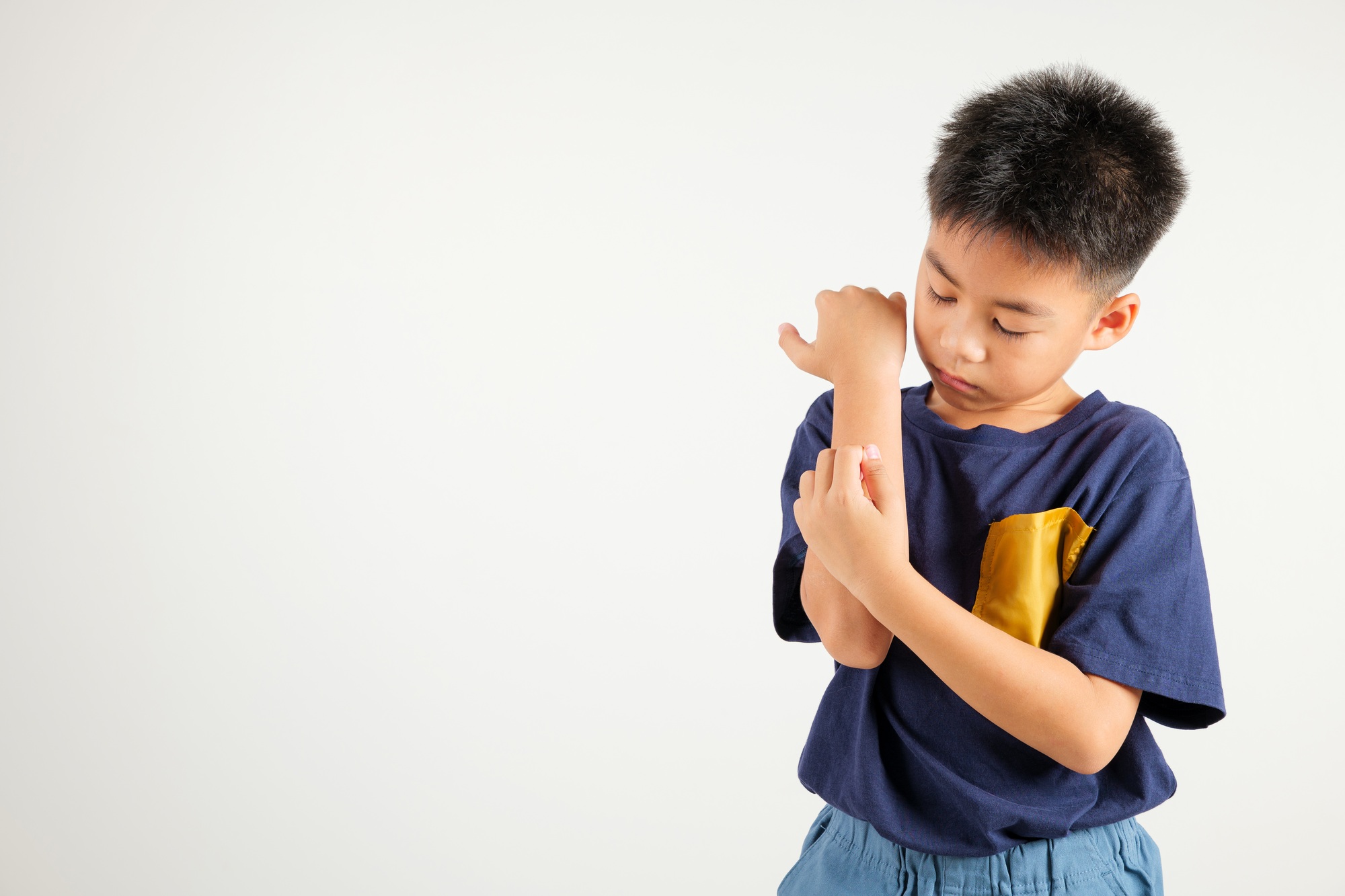 Asian little kid boy scratching itchy arm from a mosquito bite at studio shot isolated on white