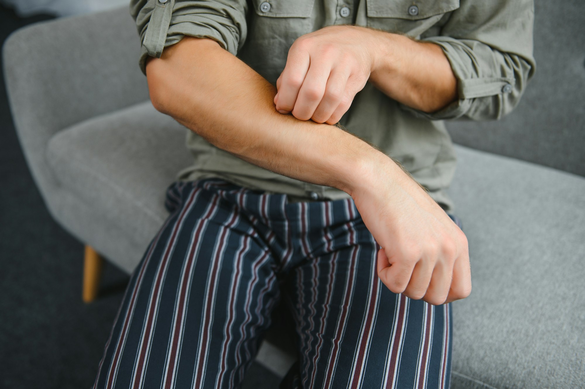 Young man scratching hand indoors, space for text. Allergies symptoms.